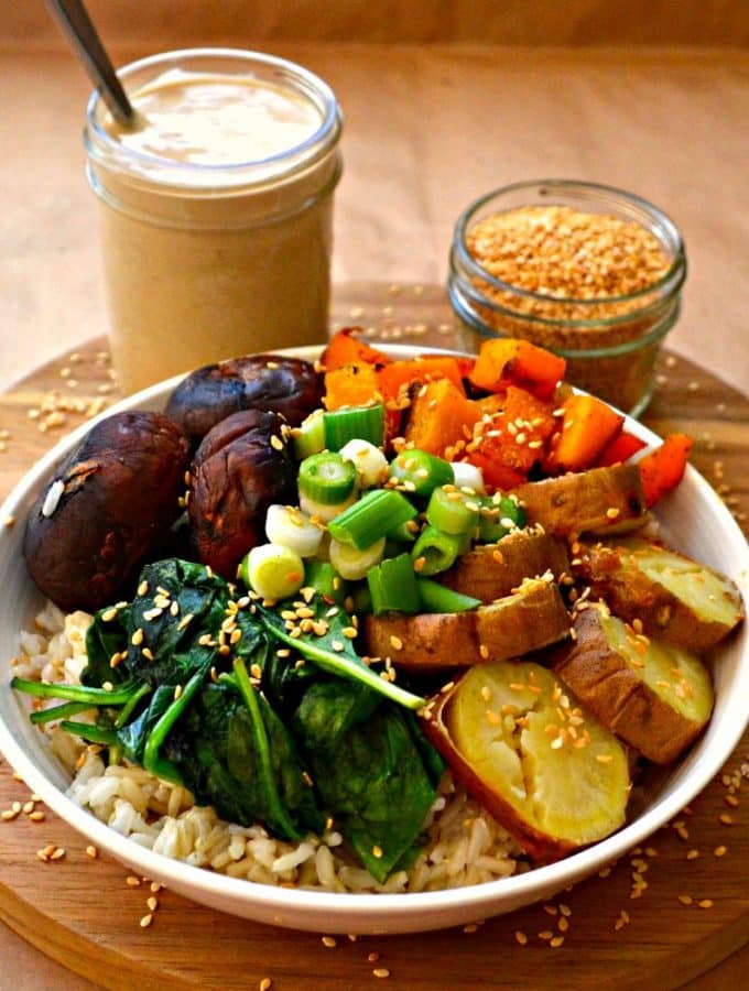 A Roasted Garlic Buddha Bowl bursting with nutty brown rice, sweet roasted vegetables,wilted greens, crunchy raw green onions, sesame seeds & heavenly roasted garlic sauce.