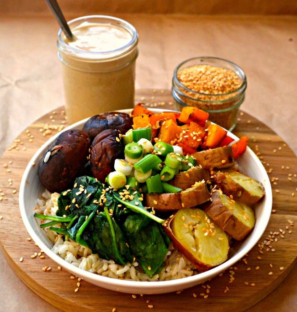 A Roasted Garlic Buddha Bowl bursting with nutty brown rice, sweet roasted vegetables,wilted greens, crunchy raw green onions, sesame seeds & heavenly roasted garlic sauce.