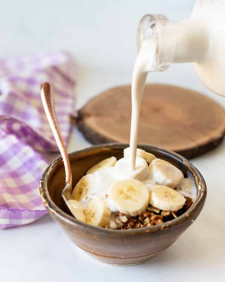 cashew milk pouring over some breakfast cereal in a bowl