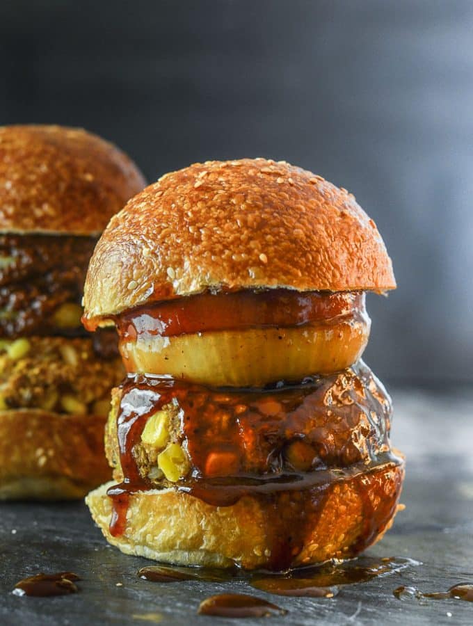 A big, thick Down Home Vegan BBQ burger in a seeded bun with an onion ring, slice of tomato and lots of BBQ sauce.