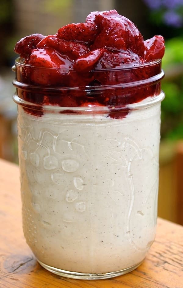 a big jar of vegan cashew cream topped with roasted strawberries