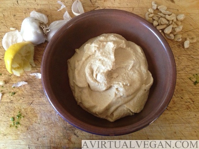 a bowl of cashew cheese sauce with garlic, cashew nuts and squeezed lemon scattered around it