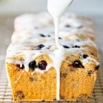 glaze being dribbled on a gluten-free lemon cake with blueberries