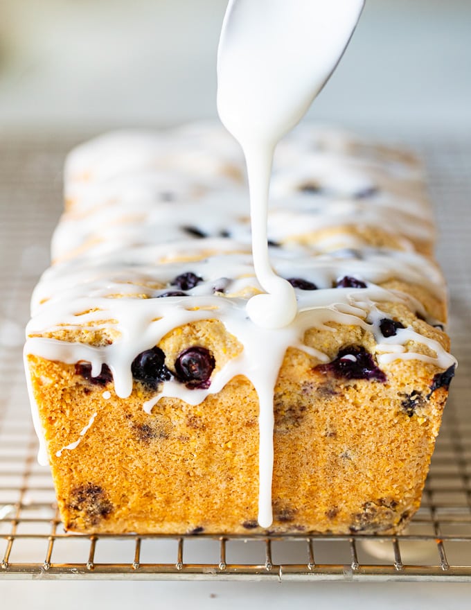 glaze being dribbled on a gluten-free lemon cake with blueberries