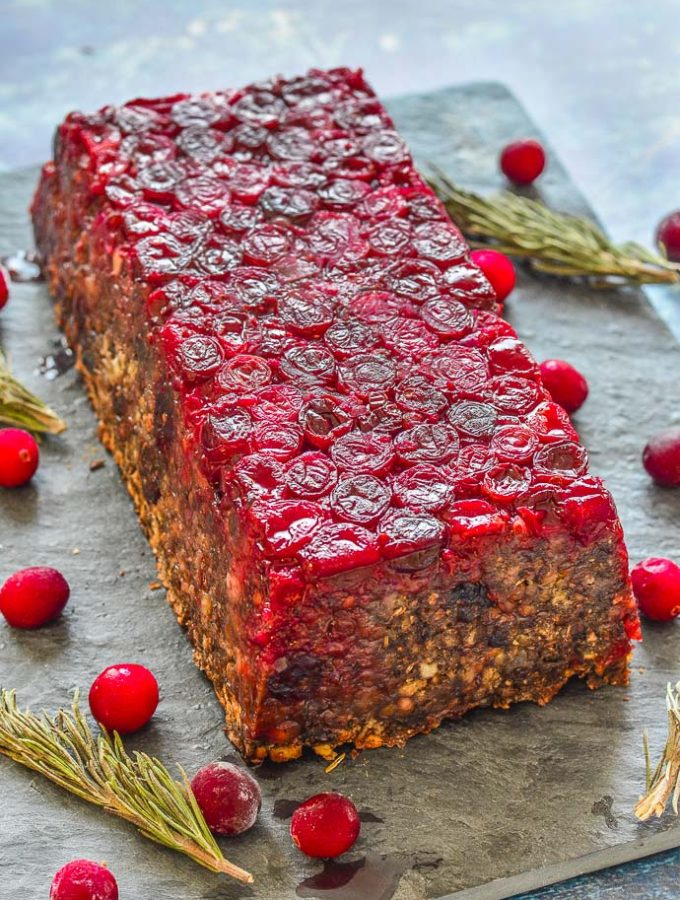 Mushroom Lentil Loaf with Cranberry topping turned out on a slate board and surrounded by scattered cranberries and rosemary