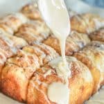 Frosting dribbling off a spoon onto freshly baked No Knead Cinnamon Pull Apart Bread