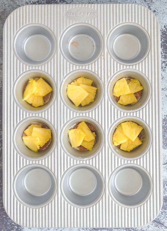 sugar and pineapple in bottom of a muffin pan ready to be covered in Pineapple Upside Down Cupcake batter