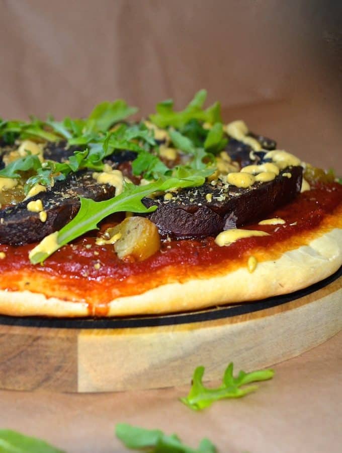 a vegan portobello and roasted garlic pizza on a round wooden board