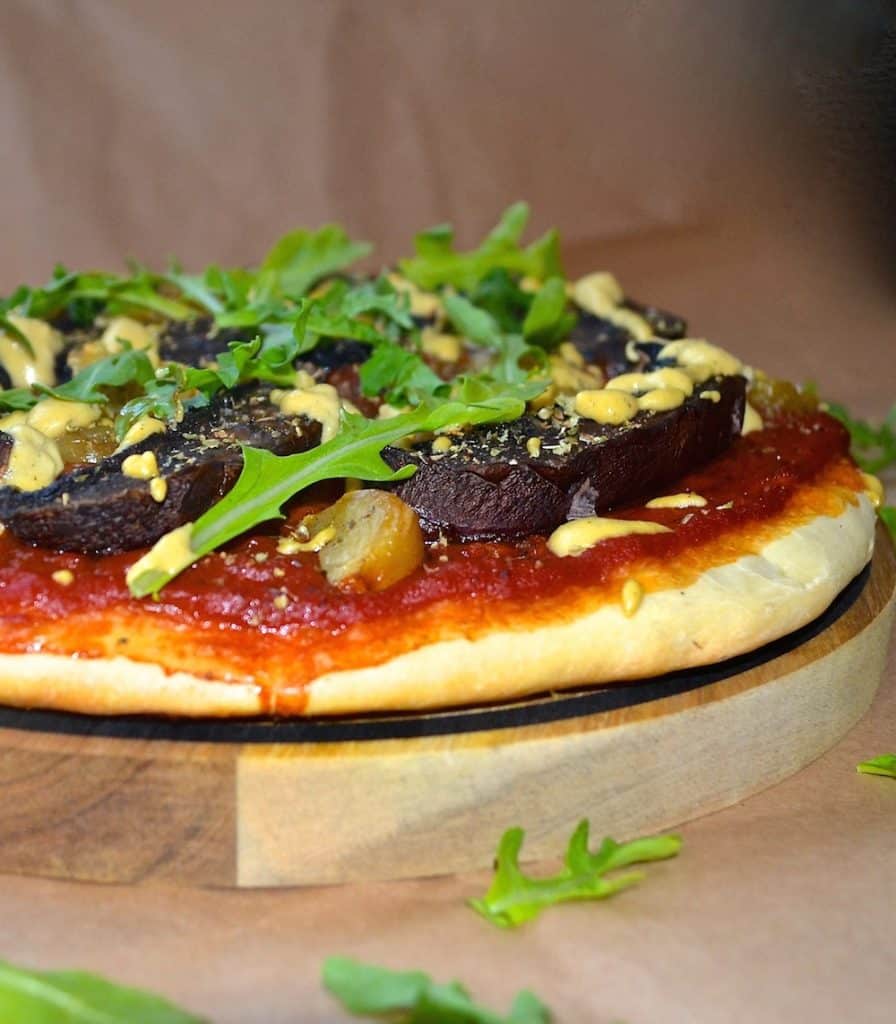 a vegan portobello and roasted garlic pizza on a round wooden board