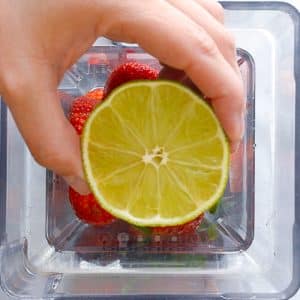 lime about to be squeezed into blender with strawberries and mint