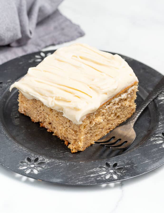 a square piece of vegan banana cake on a plate with a fork beside it