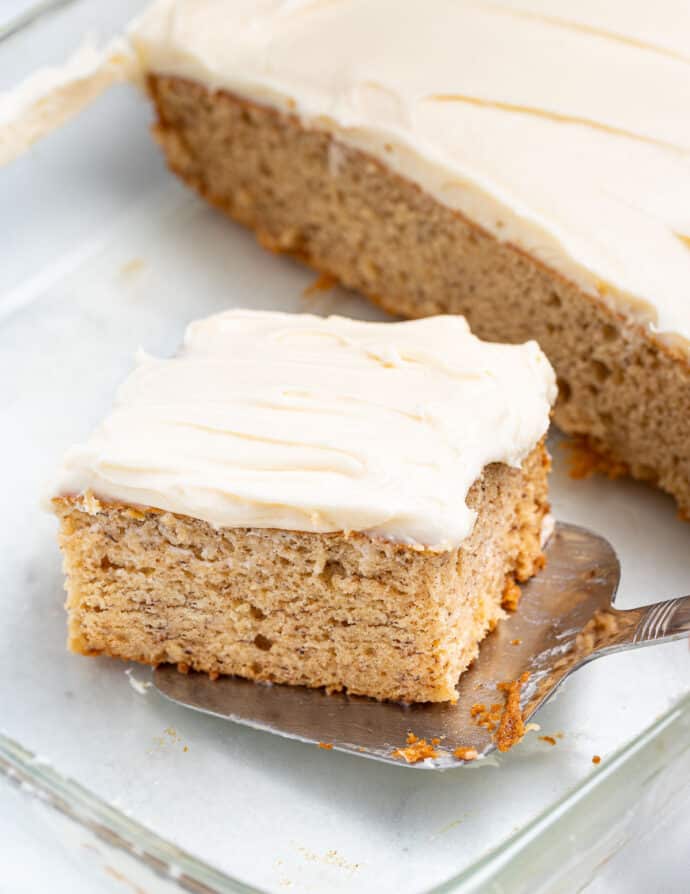 a slice of frosted banana cake being taken out of a dish