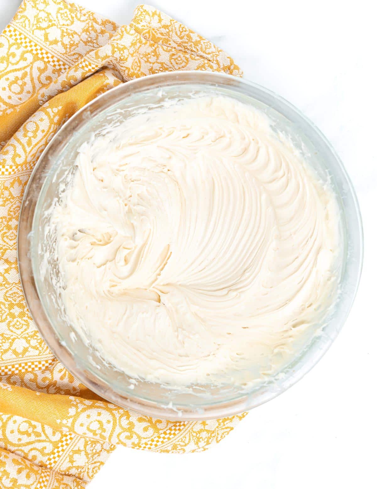 a bowl of vegan cream cheese frosting with pretty patterns from the whisk