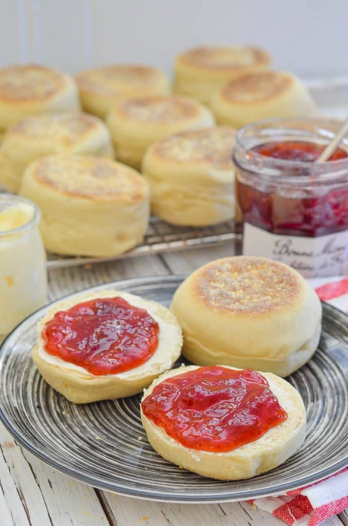 Homemade English Muffins on a plate. One split and spread with butter and jam.