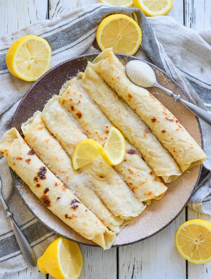 Vegan English Pancakes rolled on a plate and topped with sugar and lemon