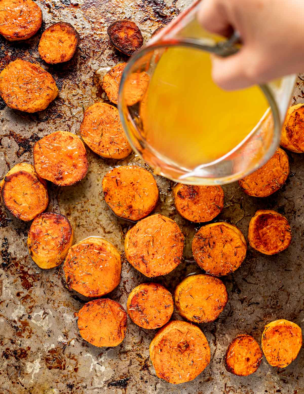 stock being poured over semi-cooked sweet potato on a baking tray